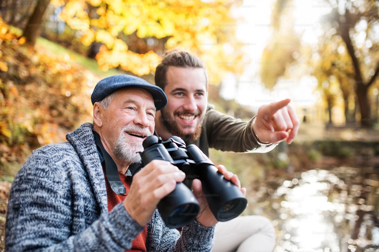 older man holder binoculars while younger man points at something